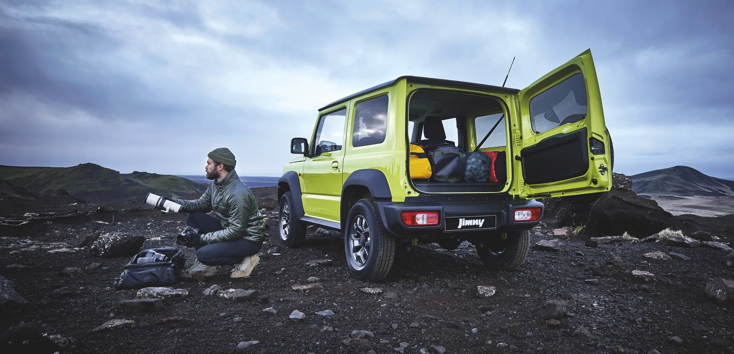 Man drinking coffee while camping beside a Suzuki Jimny