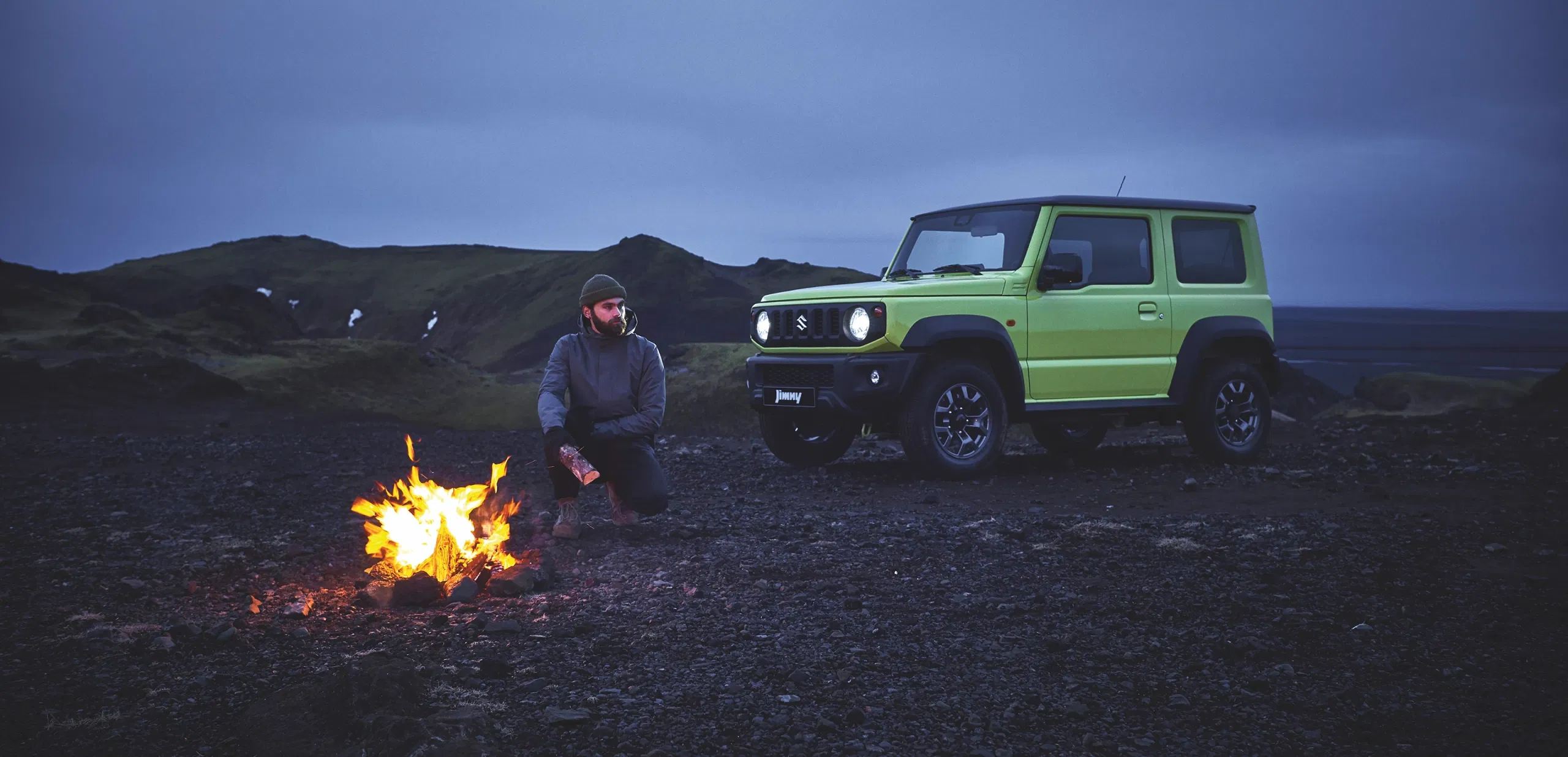 Man camping near a green Suzuki Jimny parked on rocky terrain